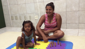 Mãe e filha sentadas sobre uma esteira de EVA no chão. Ambas estão sorrindo (Foto: Reprodução/UFCTV)