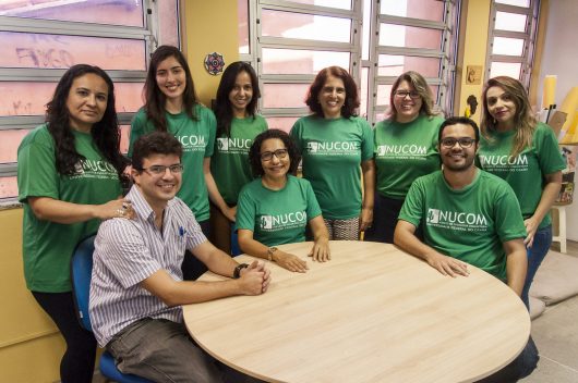 Integrantes do Nucom sentados à mesa, vestindo a blusa personalizada do grupo (Foto: Viktor Braga/UFC)