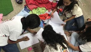 Crianças sentadas no chão em torno de papéis, onde elas desenham (Foto: Blog Divulgando a Extensão)