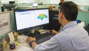 Pesquisador de costas, sentado na mesa de trabalho e usando o computador, que contém um mapa hídrico (Foto: Ribamar Neto/UFC)