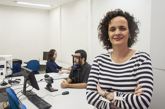 Profª Elisângela Teixeira, de brazos cruzados. Ao fundo, homem usa equipamento de eye tracking (Foto: Ribamar Neto)