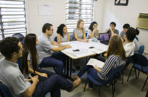 O coordenador do projeto e os estudantes ao redor de uma mesa, sentados, com projetos em papel que estão sobre a mesa (Foto: Ribamar Neto/UFC)
