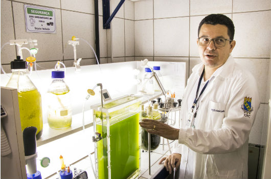 Professor André Luis Coelho ao lado de um equipamento no qual há microalgas dentro (Foto: Ribamar Neto/UFC)